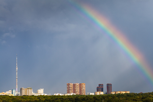 sunbeams and rainbow in rainy sky over Moscow city with TV tower and Timiryazevskiy urban park