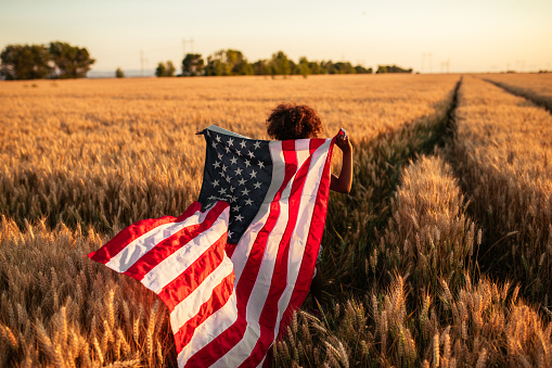 Photo of a little girl pulling an american flag in the wheat field.