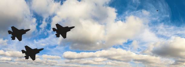 Silhouettes of three F-35 aircraft against the blue sky and white clouds stock photo