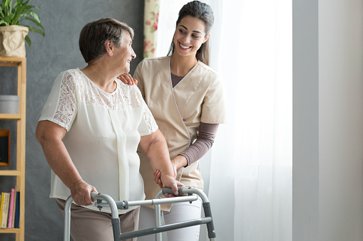 Smiling nurse helping senior lady to walk around the nursing home