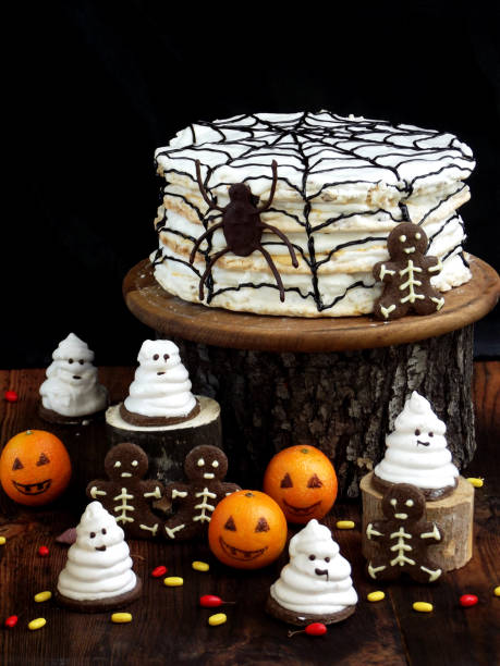 Funny delicious composition for Halloween with cake, biscuits, marshmallow and mandarins on the table. Sweets in the form of ghosts, skeletons, spiders and pumpkin jack.