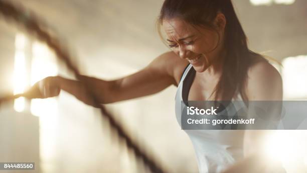 Athletic Female In A Gym Exercises With Battle Ropes During Her Cross Fitness Workout Highintensity Interval Training Shes Muscular And Sweaty Gym Is In Industrial Building Stock Photo - Download Image Now