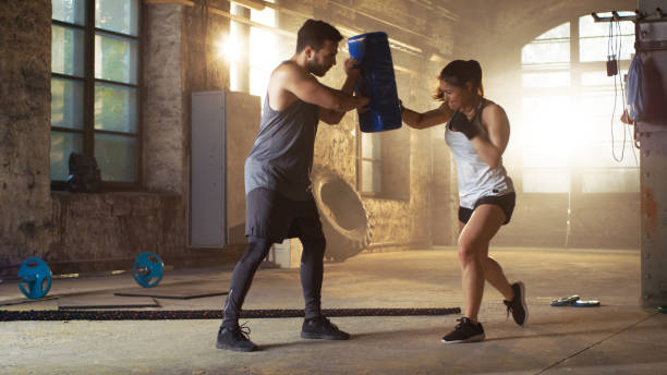 sac de boxe sport femme hits que son partenaire / formateur est titulaire. elle est chasseur professionnel et formation dans une salle de gym. - boxing winning success challenge photos et images de collection