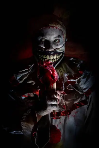 killer clown in Halloween horror house eating human heart on ice cream