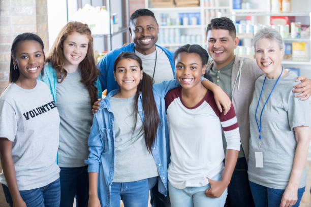 Group of diverse food bank volunteers Diverse, mixed age volunteers work together in a food bank. They are posing for a group photo and are smiling at the camera. charitable foundation photos stock pictures, royalty-free photos & images