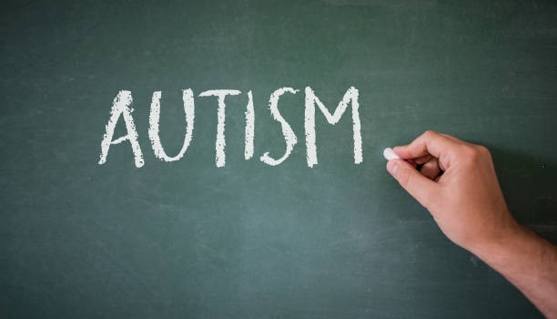 istock Hand writing on a blackboard in a class with the word AUTISM written on. 844522012