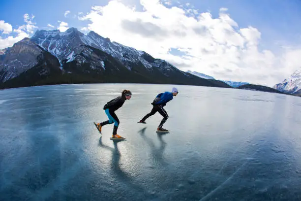 Photo of A man leads a woman on a winter speed skating adventure on Lake Minnewanka in Banff National Park, Alberta, Canada.