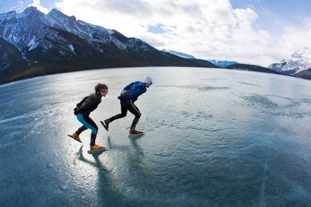 un uomo guida una donna in un'avventura di pattinaggio di velocità invernale sul lago minnewanka nel banff national park, alberta, canada. - sport winter speed skating speed foto e immagini stock