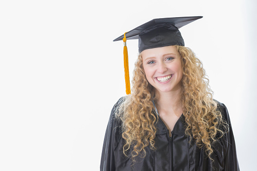 Beautiful Caucasian female high school graduate smiles confidently while wearing black cap and gown.