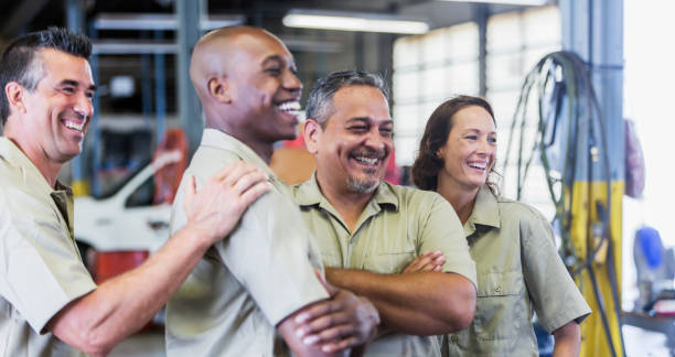 Four trucking company workers in garage Four multi-ethnic workers at a trucking company, standing in a garage, laughing. The African-American man is in his 30s. His coworkers are in their 40s, including the woman. menial job stock pictures, royalty-free photos & images