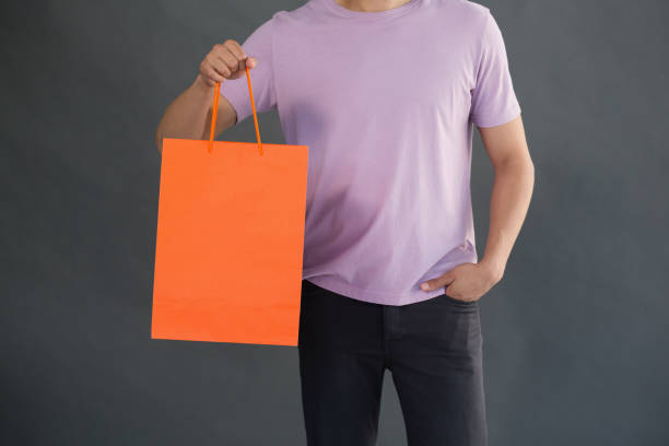 Mid-section of man holding shopping bag against grey background