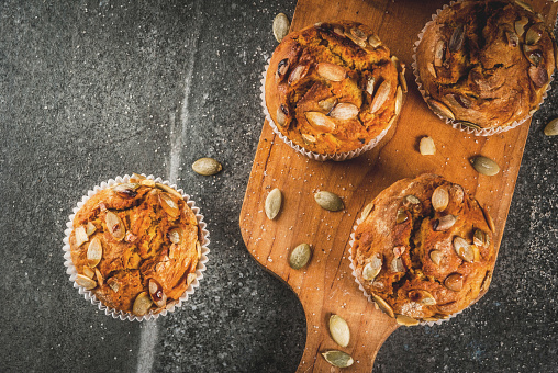 Autumn and winter baked pastries. Healthy pumpkin muffins with traditional fall spices, pumpkin seeds. Black stone table, copy space top view