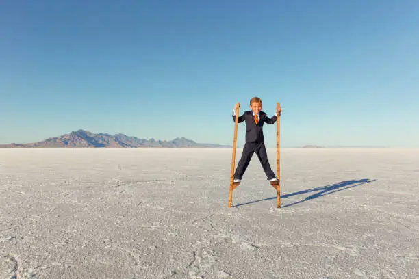 A young boy dressed as a businessman in suit is walking on stilts trying to get a leg up on his business competition and to see the business forecasting of the future. He is on stilts on the Bonneville Salt Flats of Utah, USA.