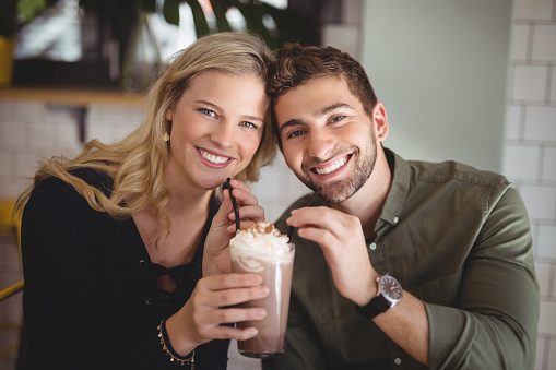 Portrait of smiling young couple holding fresh dessert in glass at coffee shop
