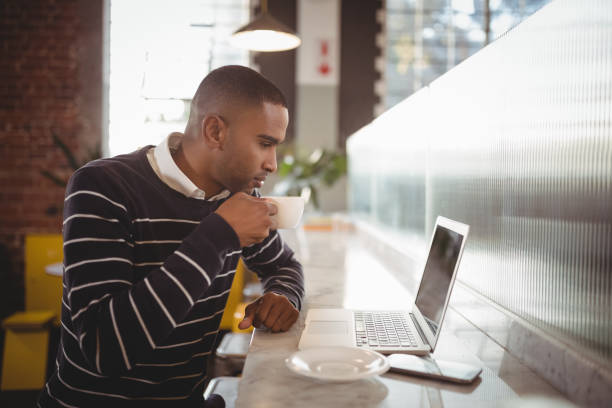 istock Side view of young man drinking coffee while looking at laptop 844784224