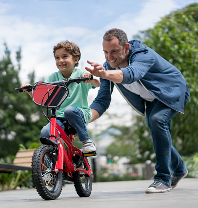 Happy boy learning to ride a bike outdoors with the help of his father - childhood concepts