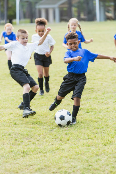 bambini che giocano a calcio, ragazzo che calcia la palla - football player group of people running american football foto e immagini stock