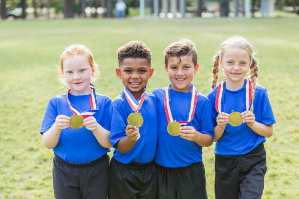 Multi-ethnic children on winning team, with medals A group of four multi-ethnic children, 6 and 7 years old, on the winning team. They are smiling at the camera, holding up the medals that are on ribbons around their necks. multi medal stock pictures, royalty-free photos & images