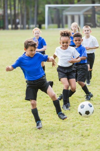 bambini che giocano a calcio, competono per la palla - football player group of people running american football foto e immagini stock