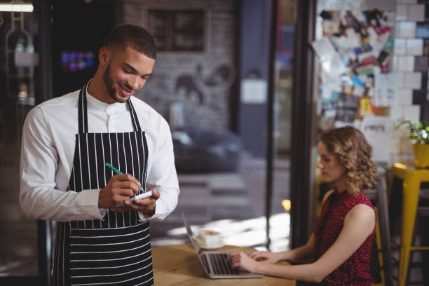 istock Smiling young waiter writing in notepad while standing at coffee shop 844814052