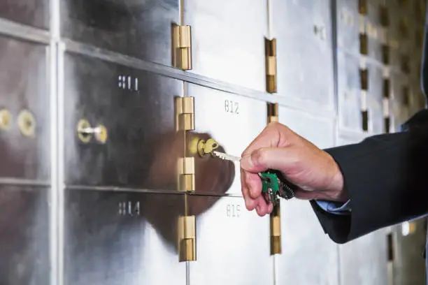 Hand of a mature man opening a safety deposit box. He is turning the key in the lock.