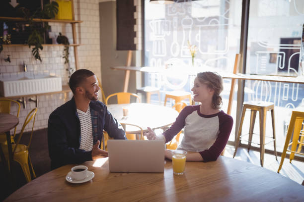 istock Smiling young friends talking while sitting with laptop at coffee shop 844818028