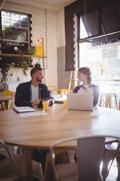 istock Smiling friends talking while sitting with technologies at coffee shop 844818338