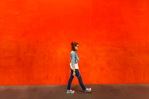 Side view of woman walking in front of wall painted with red color.