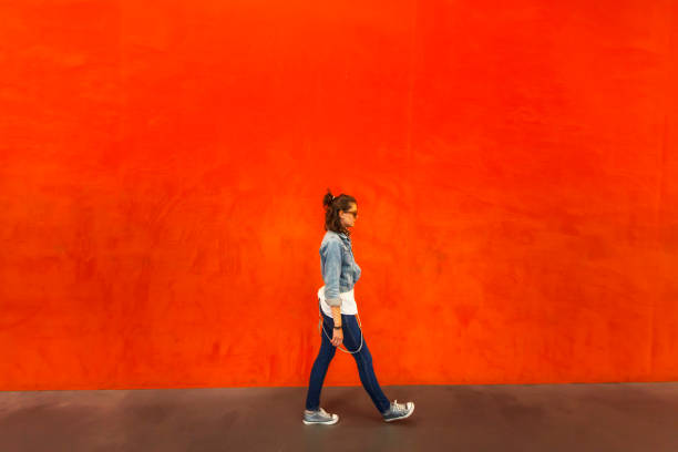 Woman walking in front of red background Side view of woman walking in front of wall painted with red color. wall sidewalk city walking stock pictures, royalty-free photos & images