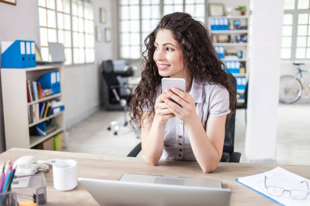 istock Smiling young woman with smart phone at workplace 844820700