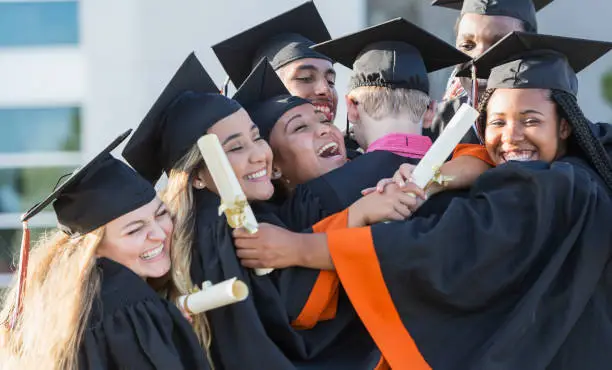 Photo of Multi-ethnic teenage graduates in cap and gown hugging