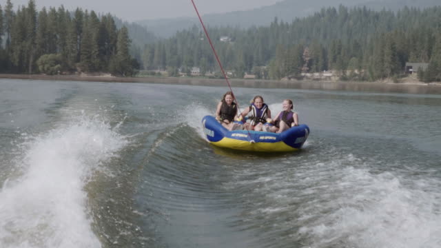 UHD 4K: Group of friends cheerfully riding an inner tube together during summer vacation