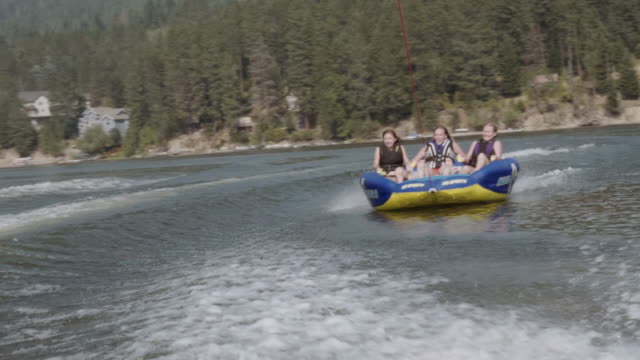 UHD 4K: Group of friends cheerfully riding an inner tube together during summer vacation