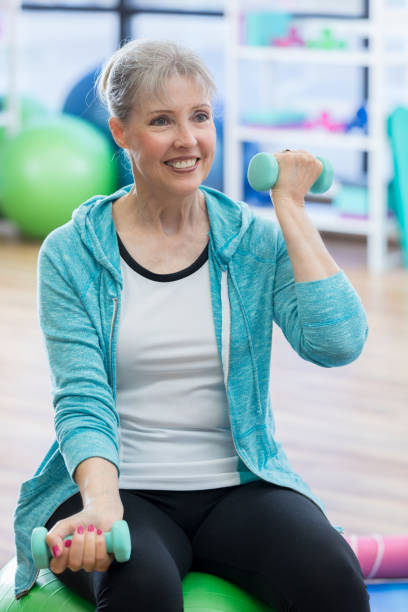 istock Smiling senior woman sits on exercise ball while lifting weights 844928380