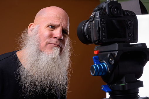 Studio shot of bald man with long gray beard getting ready for vlogging against colored background horizontal shot