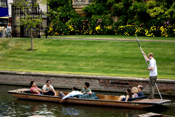 Punting on the River Cam A group of tourists of mixed ethnicity on a punt on the River Cam in Cambridge, England. Cambridge is famous for punts and is one of the two premiere University towns in the UK. This is being punted by an official tour guide as part of a rental package. couple punting stock pictures, royalty-free photos & images