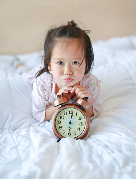 istock Cute little girl with alarm clock lying on bed. 845064108