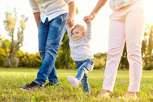 The first steps of the baby. Parents are teaching their child to walk. A happy family.