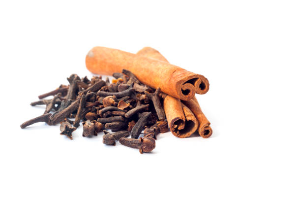 Two cinnamon sticks and a pile of dried cloves cloves on a white background Two cinnamon sticks and a pile of dried cloves cloves on a white background clove spice photos stock pictures, royalty-free photos & images