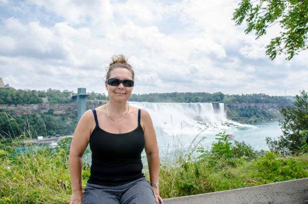 Tourist woman on a ledge overlooking a waterfall with a rainbow next to it.