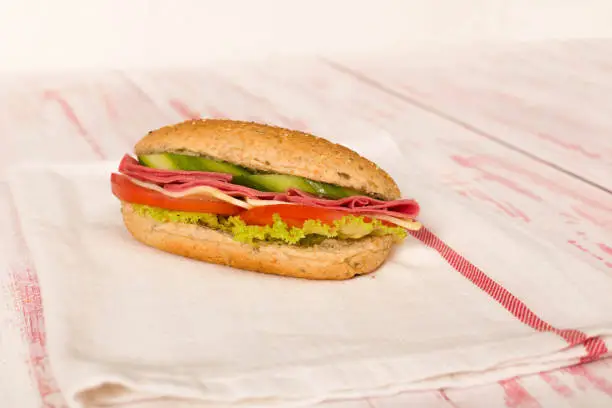 Photo of Sandwich with cheese, tomato, salami, cucumber and lettuce on wooden table