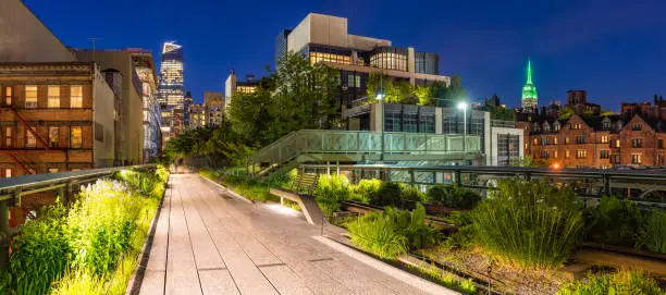 Panoramic view of the High Line promenade at twilight with city lights and illuminated skyscrapers. Chelsea, Manhattan, New York City