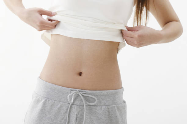 Flat female belly with moles. Beautiful body with birth marks of young woman isolated on gray studio background. Fit, healthy and slim authentical body. Natural beauty, treatment, healthcare