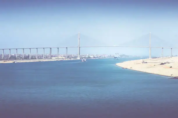 The Suez Canal at El-Qantara with ships and Mubarak Peace Bridge in hazy sunlight