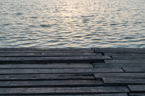 istock Sunlight in sunset time reflection on water wave in lake with wood floor 845213612