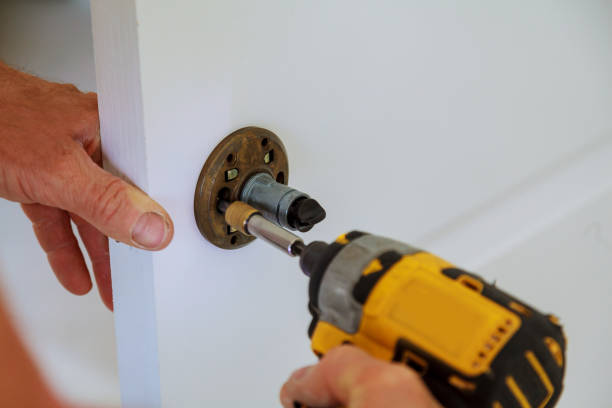 istock Installation of door lock using a screwdriver to. Carpenter at lock installation with electric drill into wood door. 845273996