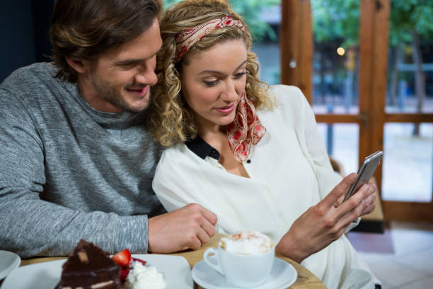 istock Loving couple using smart phone at table in cafeteria 845280356