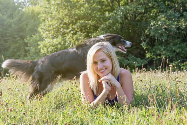 istock Smiling young woman is lying in the grass while her Border Collie skips her 845290188