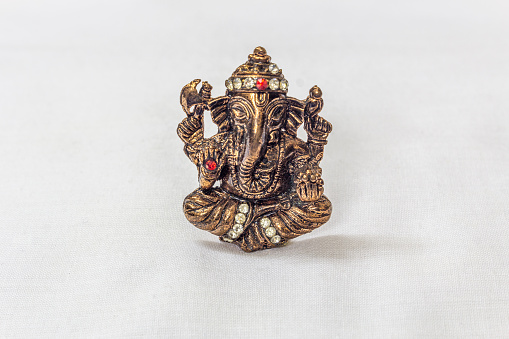 Brass carved lord ganesha idol in metallic colour with artificial stone carvings in a white backdrop. Macro with extremely shallow depth of field with selective focus on the subject.