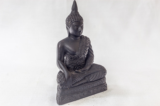 Moulded buddha idol in complete black colour in a white backdrop. Macro with extremely shallow depth of field with selective focus on the subject.